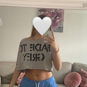 Grå croppad t-shirt från Monki - Säljer en grå croppad t-shirt från Monki med svart text 'FADE TO GREY' på framsidan. T-shirten har korta ärmar och en avslappnad passform, perfekt för en chill och trendig look.