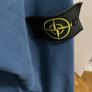Blå sweatshirt från Stone Island - Säljer en blå sweatshirt från Stone Island med klassisk logotyp-patch på vänster ärm. Tröjan har rund halsringning och ribbade muddar vid ärmslut och nederkant. Perfekt för en stilren och avslappnad look.