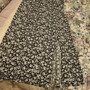 Svartvit blommig långklänning från Amisu - Säljer en svart kjol  från Amisu med vitt blommönster. Och har slits framtill och är i ett lätt material, perfekt för varmare dagar. Stängs med dragkedja i sidan. Superfin till sommaren!