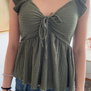 grön topp med knyt - Säljer en gröntopp med v-ringning och knyt framtill. Toppen har volangärmar och ett lätt, luftigt tyg . Skitt snugh