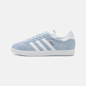 Ljusblå Adidas Gazelle sneakers - Säljer ett par ljusblå Adidas Gazelle sneakers med klassiska vita ränder och vit sula. Skorna har snörning och är tillverkade i mocka med detaljer i syntet. Perfekta för dig som gillar stilrena och tidlösa sneakers. Det är i väldigt fint skick. Nypriset var 1400kr