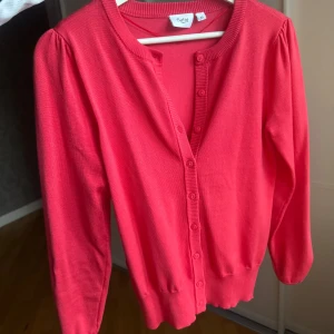 Röd kofta från Saint Tropez - Säljer en söt rosa kofta från Saint med rund halsringning och knäppning framtill. Koftan har långa ärmar och ribbade muddar vid ärmslut och nederkant. Perfekt att slänga över en topp eller klänning.