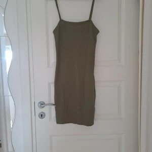 Olivgrön ribbad klänning från Amisu - Säljer en olivgrön ribbad klänning från Amisu med smala axelband och figurnära passform. Klänningen är kort och har en enkel, stilren design som passar perfekt till sommaren.