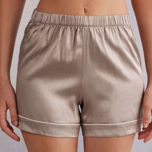 Beige satinshorts med resårmidja - 🇸🇪Snygga beige shorts i satin med elastisk midja och diskret vit kant nertill. Perfekta för en chill och stilren look. Lätta och sköna med en normal passform.🇫🇮Intimissimi shortsit. Istuu hyvin.