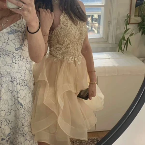 Champagnefärgad festklänning med spets och volang - 🇸🇪Säljer en champagnefärgad klänning med vacker spets upptill och volangig kjol. Klänningen har smala axelband och är ärmlös, perfekt för bal eller fest. Kjolen är kort och har flera lager för extra volym.🇫🇮 Rippimekko tai synttäri. Menee 34-36 koolle, myös pienelle 38 kokoiselle. Käytetty kerran. ”Ompelijalla” teetetty.