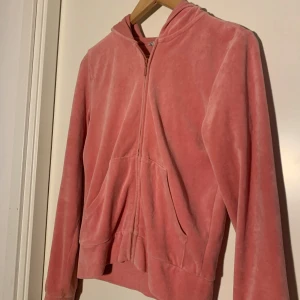 Rosa velour hoodie - Mysig rosa hoodie i mjuk velour med dragkedja framtill och huva. Tröjan har långa ärmar och två fickor framtill. Perfekt för en avslappnad och bekväm stil.