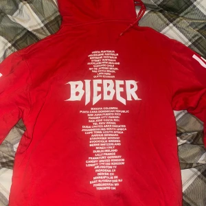 Röd Bieber hoodie med tour-tryck - Röd hoodie med vit text och tryck från Justin Biebers turné. Tröjan går inte att köpa längre så ganska ovanlig. 