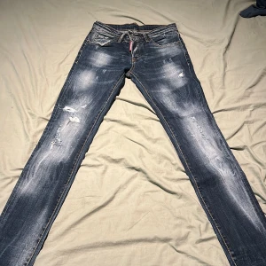 Blå slitna jeans från Dsquared2 - Säljer ett par blå jeans från Dsquared2 med slitningar och snyggt tvättad look. Jeansen har klassisk femficksmodell, dragkedja och smal passform. Perfekta för dig som gillar en trendig och avslappnad stil.