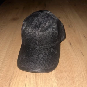 Svart keps  med -mönster - Säljer en svart keps från  med diskret GGmönster över hela kepsen. Justerbar rem baktill för perfekt passform. Snygg och stilren design som passar till många outfits.