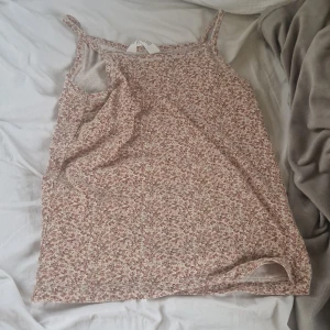 Blommig linnetopp i beige och rosa - Söt linnetopp med smala axelband och blommigt mönster i beige och rosa toner. Perfekt för varma dagar och enkel att matcha med jeans eller kjol.