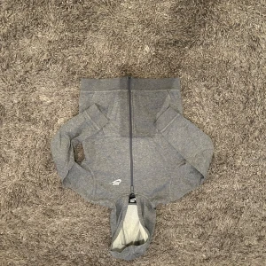 Grå hoodie med dragkedja från Nike - Säljer en grå zip-hoodie från Nike med broderad logga på bröstet. Tröjan har långa ärmar, huva och mjukt foder på insidan. Perfekt för en avslappnad stil och enkel att matcha med det mesta.