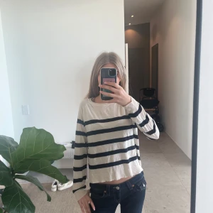 Randig croppad långärmad tröja - Säljer en vit långärmad tröja med svarta horisontella ränder. Tröjan är croppad och har en avslappnad passform. Perfekt för en enkel och stilren look.