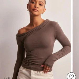 Brun one shoulder topp - Säljer en brun långärmad topp med one shoulder-design. Toppen är tight och har en snygg asymmetrisk skärning över axeln. Perfekt för dig som vill ha en stilren och trendig look.