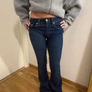 Mörkblå bootcut jeans - Säljer ett par mörkblå bootcut jeans med låg midja och klassiska fickor bak. Jeansen har en snygg passform och stängs med dragkedja och knapp framtill. Perfekta för dig som gillar en retroinspirerad stil. Dessutom sydda lågmidjade 