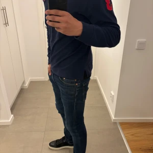 Mörkblå långärmad tröja från Polo Ralph Lauren - Säljer en mörkblå långärmad tröja från Polo Ralph Lauren i storlek XS. Tröjan har en klassisk passform och röd detalj på ärmen. Perfekt för en stilren och avslappnad look.