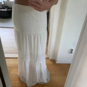 Vit långkjol med broderade hål - Säljer en vit långkjol med broderade hål i blommönster. Kjolen har en luftig och flowy passform med volangdetalj nedtill. Perfekt för varma dagar och ger en romantisk känsla till outfiten. Obs lite smutsig nedtill då den skrapat i marken😊Barnstorlek 158-164