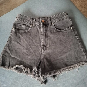 Grå jeansshorts med fransar från Divided - Gråa jeansshorts från Divided med hög midja och fransar längst ner!