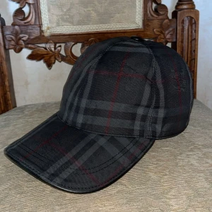 Svart rutig keps från Burberry - Snygg svart keps från Burberry med klassiskt rutigt mönster i grått och rött. Justerbar rem baktill med Burberry-logga. Perfekt accessoar för en stilren look.