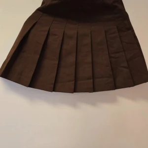 Brun plisserad kjol från H&M Divided - Säljer en brun plisserad kjol från H&M Divided i storlek 32. Kjolen har klassiska veck och en kort passform som ger en snygg och trendig look. Perfekt att styla med en enkel topp eller stickad tröja. Den är bara upptvättad aldrig använt 