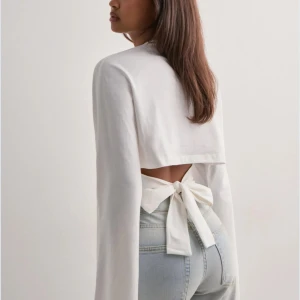 Vit långärmad topp med rosett i ryggen - Säljer en vit långärmad topp med vida ärmar och snygg rosettdetalj i ryggen. Aldrig använd! (PRISLAPP KVAR PÅ TRÖJAN) 