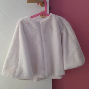 Vit pälsjacka för dam - Säljer en fluffig och mjuk vit pälsjacka med lång ärm. Jackan har en enkel och stilren design utan synliga detaljer framtill. Perfekt för att ge en lyxig känsla till din outfit.