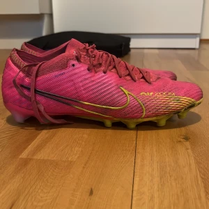 Nike Mercurial rosa fotbollsskor - Säljer ett par Nike Mercurial fotbollsskor i en riktigt snygg rosa färg med gula detaljer och svart swoosh. Använda en säsong men inga skador. Skorna är elite så väska kommer med
