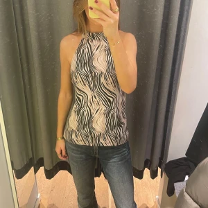 Mönstrad halterneck topp - Säljer en snygg halterneck topp med vågigt zebramönster i svart, beige och vitt. Toppen är ärmlös och är även helt öppen i ryggen (man knyter den bak). Toppen har ett satängliknande material som är perfekt till sommaren☀️