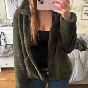 Olivgrön pälsjacka - Säljer en olivgrön pälsjacka med krage och fickor. Jackan är mjuk och har en klassisk passform som funkar till många olika outfits. Perfekt för dig som vill ha en mysig och snygg jacka till hösten eller vintern.