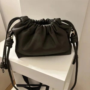 olivgrön  axelväska med dragsko - Snygg olivgrön  axelväska i skinn med dragsko och knutna detaljer på axelremmen. Perfekt för en stilren look och enkel att matcha med olika outfits.