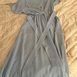 Ljusblå omlottklänning från SHEIN - Säljer en ljusblå omlottklänning från SHEIN i storlek XS. Klänningen har korta ärmar, v-ringning och ett knytband i midjan som ger en fin siluett. Perfekt för vår och sommar, med en luftig och mjuk känsla.