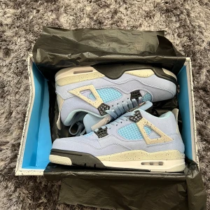 Nike Air Jordan 4 University Blue - Pris kan diskuteras vid snabb affär! Säljer ett par helt nya, oanvända Nike Air Jordan 4 i färgen University Blue. Skorna har ljusblå mocka, vita och svarta detaljer samt meshpaneler på sidorna. Sulan är vit med svarta och blå inslag, och de har klassisk snörning och Jordan-logga på plösen. 