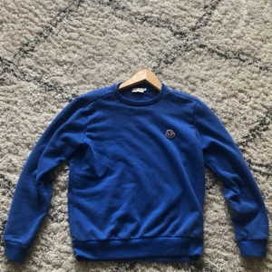 Blå sweatshirt från Moncler - Säljer en klassisk blå sweatshirt från Moncler med rund halsringning och broderad Moncler-logga på bröstet. Tröjan har långa ärmar och ribbade muddar vid ärmslut och nederkant. Perfekt för en stilren och avslappnad look.