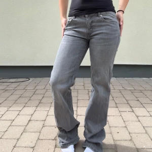 Grå lågmidjade jeans med bootcut - Säljer ett par grå lågmidjade jeansbyxor med utsvängda ben och klassiska fickor både fram och bak. Byxorna har normal passform och är i full längd. Perfekta för dig som gillar en enkel och stilren look.