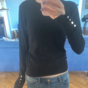 Svart långärmad tröja med knappar på ärmarna - Säljer en svart snygg helt vanlig tröja med knappar vid armarna. (Tröjan har inga fläckar utan det är spegeln) 