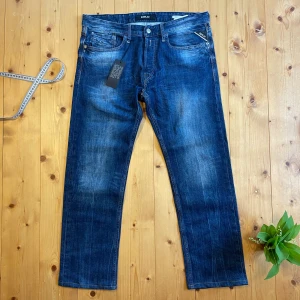 Replay Newbill jeans i blå denim - Säljer ett par klassiska blå jeans från Replay, modell Newbill. Jeansen har raka ben, fem fickor och snygga slitningar framtill. Märkesdetaljer på bakfickan och läderpatch i midjan. Perfekta för en avslappnad stil. Jeansen är helt nya och riktigt snygga. Hör av dig om du har frågor🤙