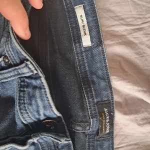 Blå slim jeans från Jack & Jones - Säljer ett par klassiska blå slim fit jeans från Jack & Jones. Jeansen har knäppning med knappar och tydliga sömmar. Perfekta för dig som gillar en smalare passform och tidlös denimstil.