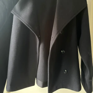 Svart kappa från Gina Tricot - Säljer en svart kappa från Gina Tricot i storlek 146-152. Jackan har stora slag och knäpps med knappar framtill. Perfekt för kyligare dagar och passar till många olika outfits. 146-152=xs