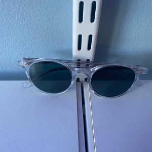 Transparenta solglasögon från TBD Eyewear - Snygga solglasögon med transparent båge och mörka runda linser från TBD Eyewear. Modellen heter CRAN och har en stilren och modern design som passar perfekt till sommaren. Små repor förekommer men allmänt i bra skick. Säljer då de ej kommer till användning.