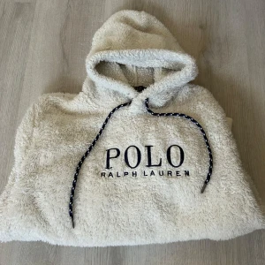 Vit fleece hoodie från Polo Ralph Lauren - Mysig vit hoodie från Polo Ralph Lauren i fluffig fleece. Stor broderad logga framtill, huva med dragsko och stor magficka. Perfekt för kalla dagar när du vill vara både bekväm och snygg.