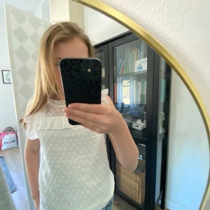 Vit blus med volang från SHEIN - Söt vit blus från SHEIN med små prickar i tyget och volangdetaljer vid axlar och bröst. Blusen är ärmlös och har en lätt transparent känsla med en liten v-ringning fram. Perfekt för vår och sommar!Storlek XS/S!💕💕💕💕