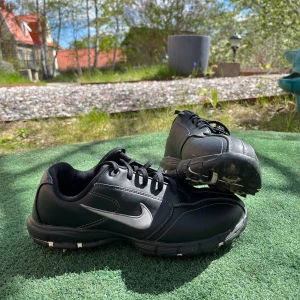 Golfskor Nike - Säljer ett par svarta golfskor från Nike med vit swoosh på sidan. Skorna har snörning och rund tå, samt dobbar under sulan för bra grepp. Själva skorna är i bra skick, några av dubbarna är inte lika bra men går att byta om man vill. Skulle inte säga att det alls behövs dock 