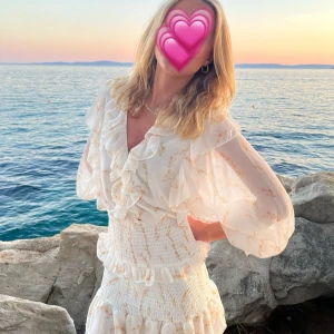 Klänning med volanger  - Från Australiska märket Sabo Skirt, nypris 1500kr. Supersöt vit kortklänning med volangdetaljer och v-ringning. Klänningen har långa, luftiga ärmar, smock detalj längst ut på dem och smockad midja med en öppning framstill där ”kjolen” börjar. Man kan dra upp kjolen som jag gjort här för jag ej ville visa magen, eller dra ner lite:) vid snabbaffär kan pris diskuteras💗 