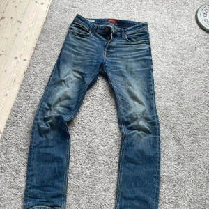 Blå jeans från Jack & Jones Slim Straight Tim - Säljer ett par klassiska blå jeans från Jack & Jones, modell Slim Straight Tim. Jeansen har fem fickor, normal passform med raka ben och snygga slitningar framtill och baktill. Perfekta till vardags och lätta att matcha med olika stilar.