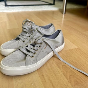 Grå sneakers från gant - Säljer ett par stilrena grå sneakers från gant. Jag har enbart använt de när jag testat de utomhus, därav är de i princip som nytt skick. Skorna har klassisk snörning och är tillverkade i textilmaterial. Köptes för 1500kr.