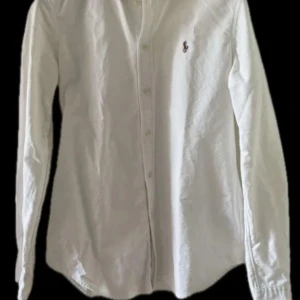 Vit skjorta från Ralph Lauren - Klassisk vit skjorta från Ralph Lauren med broderad logga på bröstet. Skjortan har lång ärm, knappar framtill och är i modellen Custom Fit.  Perfekt till många olika tillfällen och enkel att matcha. Skriv för fler bilder eller om ni har frågor