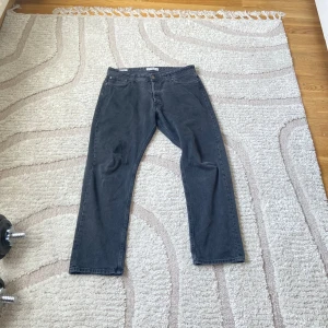 Mörkgrå Jack Jones jeansbyxor - Säljer ett par mörkgrå jeansbyxor från Authentic Jeans Wear i klassisk rak modell. Byxorna har fem fickor, bälteshällor och stängs med dragkedja och knapp. Perfekta för en avslappnad stil.
