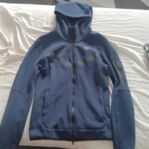 Blå hoodiejacka från nike - Säljer en blå hoodiejacka från Nike med dragkedja framtill och huva. Jackan har långa ärmar och två fickor framtill. Perfekt för träning eller som en sportig vardagsjacka.