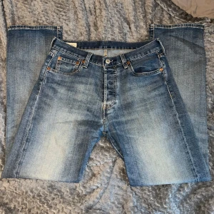 Levi's 501 jeans i blå denim - Klassiska blå Levi's 501 jeans med raka ben och knappgylf. Jeansen har en snygg tvätt med ljusare partier framtill och bakficka med den ikoniska röda Levi's-lappen. Perfekta för en avslappnad stil.