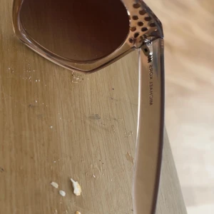 Bruna solglasögon med nitar från Michael Kors - Snygga solglasögon från Michael Kors i transparent brun plast med fyrkantig form. Bågarna har dekorativa guldfärgade nitar vid sidorna för en extra touch. Mörka glas som ger ett coolt intryck.