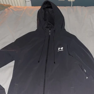 Under Armour windbreaker  - Hej! Jag säljer en oanvänd under armour jacka eftersom jag beställde fel storlek. Den är i storlek M. Jackan är väldigt snygg och passar perfekt nu till sommarkvällar och självklart under våren och hösten med. Pris kan diskuteras. KVITTO FINNS 